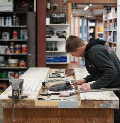 Timmerman van Van Wiggen Bouw schuurt een houten onderdeel in de werkplaats tijdens de voorbereiding van een bouwproject