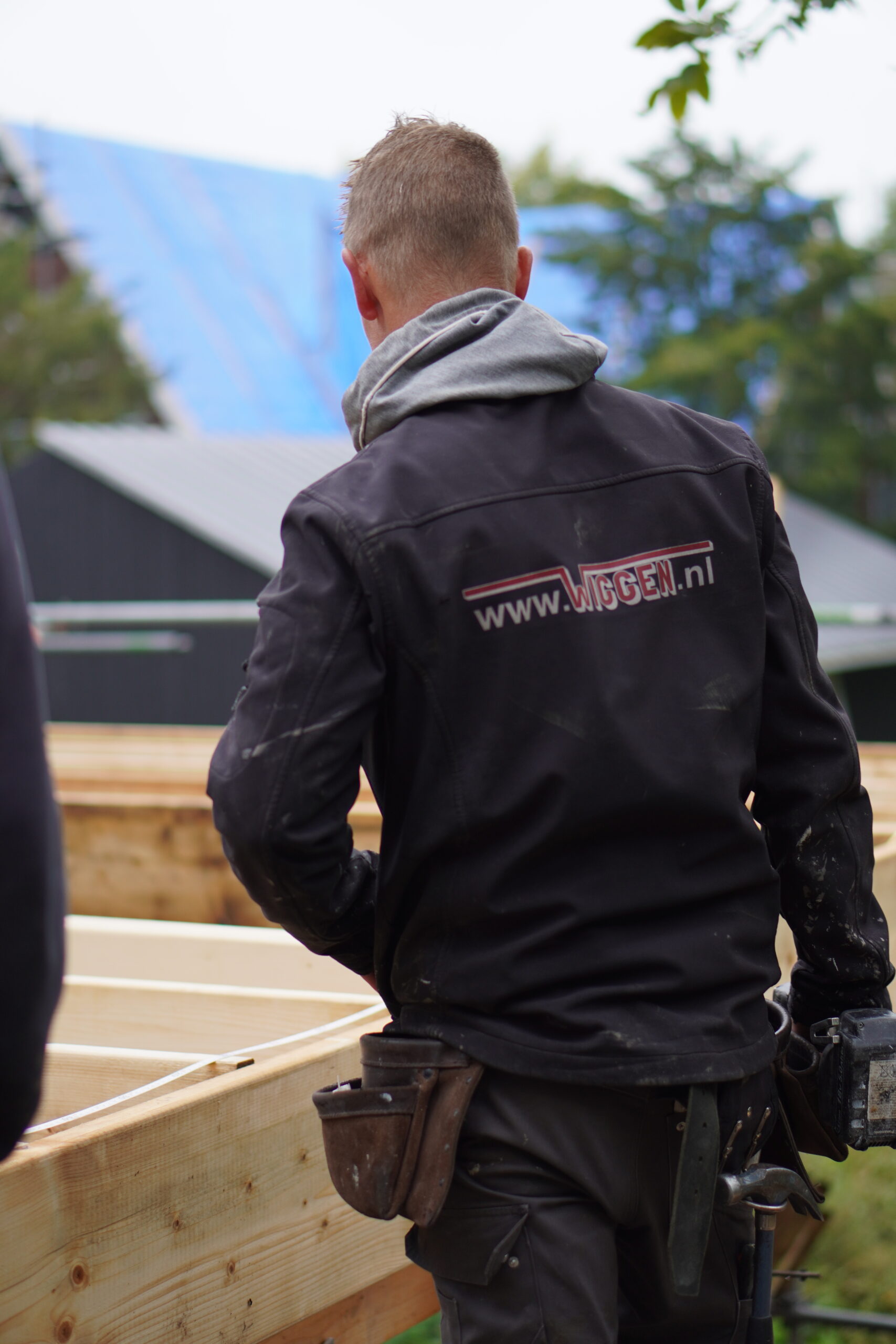 Voorman van Van Wiggen Bouw aan het werk op de bouwplaats, lachend tijdens het plaatsen van houten constructiedelen